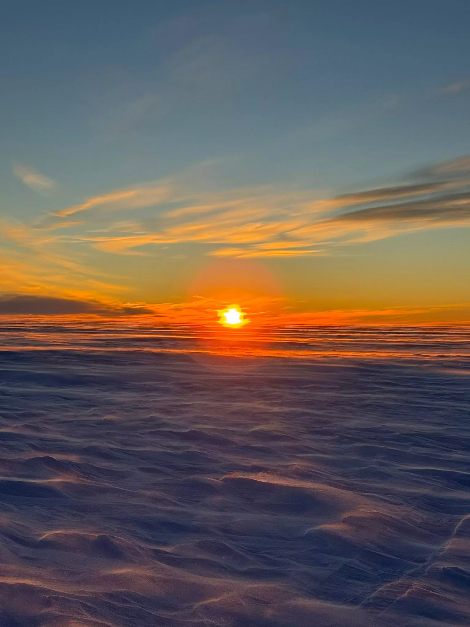 Sonnenaufgang in einer Schneelandschaft in der Antarktis. Dazu Wolkenformationen in orange angestrahlt